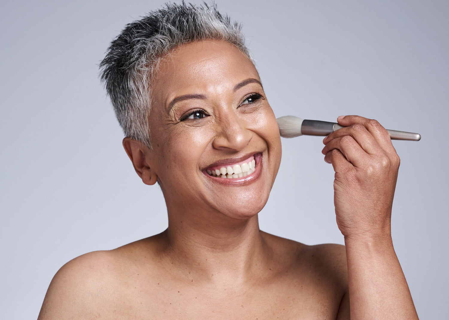 Woman holding a makeup brush against a plain background