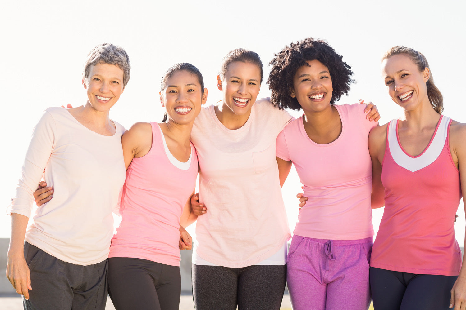 Five women posing together outdoors, wearing pink and white athletic wear.