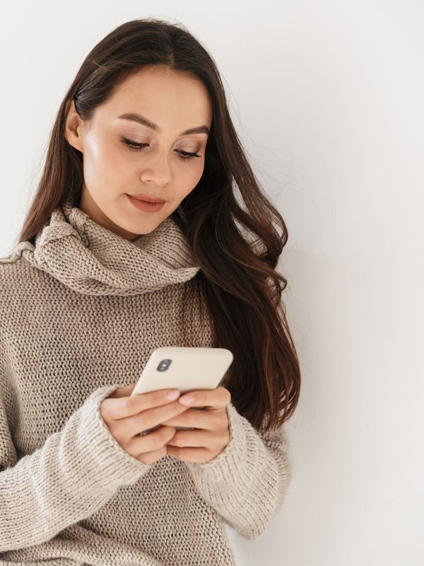 Woman in a beige sweater and scarf using a smartphone against a white background