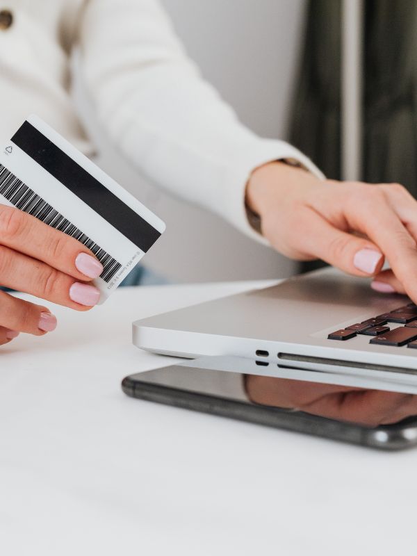 Person holding a credit card and using a laptop on a white surface
